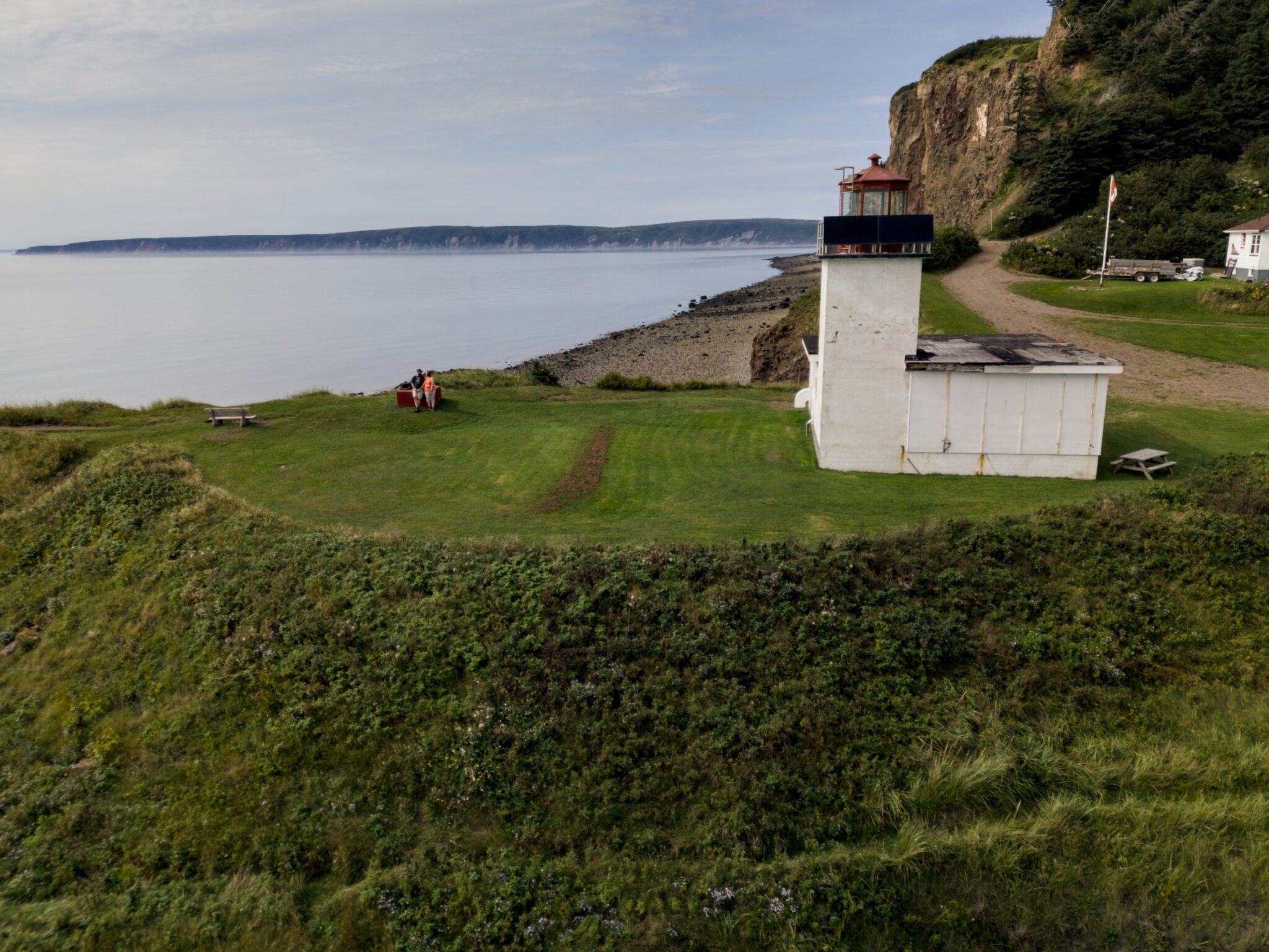An aerial view of a lighthouse beside coastal cliffs and calm water.
