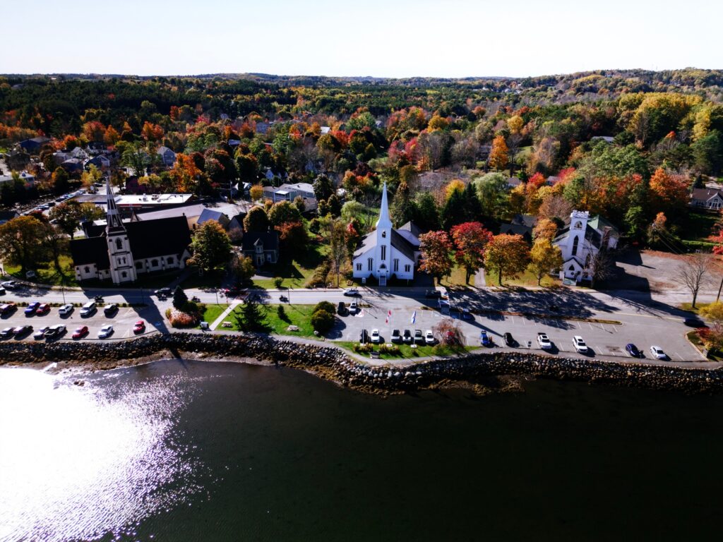 A waterfront town with churches and autumn trees viewed from across the river.