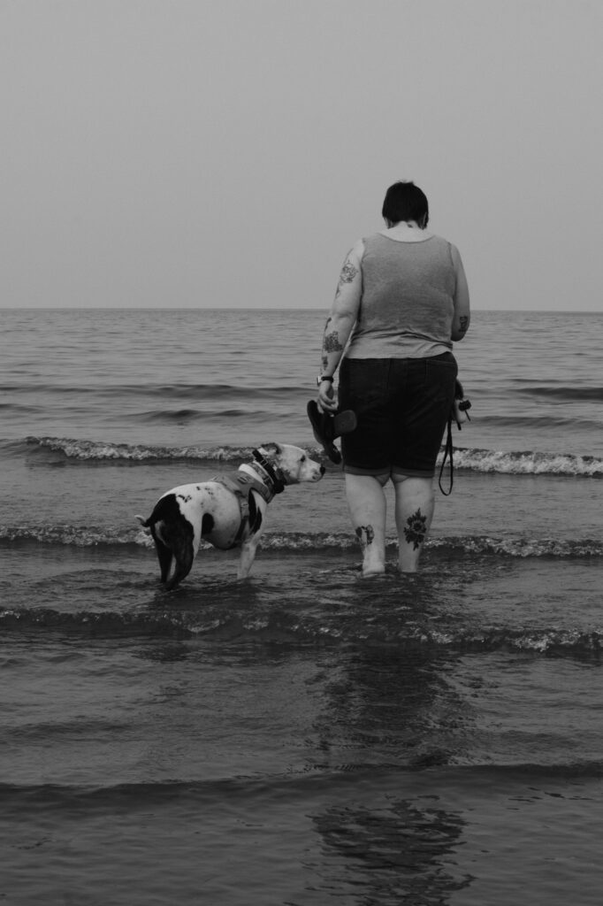 A person and dog share a quiet moment beside the water.